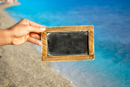 Hand holding blank blackboard with sea  in backgroundの写真素材