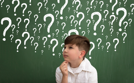 Little boy thinking surrounded question marks on chalkboardの写真素材