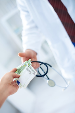 Doctor's hand in glove receives money, concept corruption in health careの写真素材