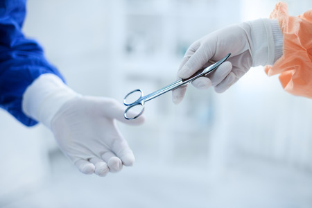 Assistant gives scissors for operation to surgeonの写真素材