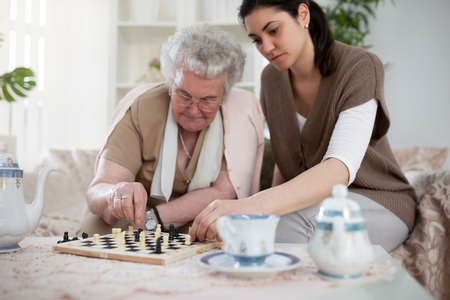 Old woman playing chess with young womanの写真素材