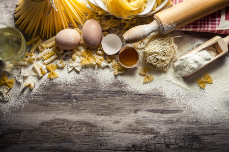 Mixed pasta with eggs and rolling pin on floured wooden surfaceの写真素材