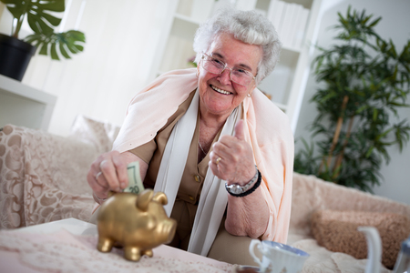 Old woman is putting money in piggybank for her pensionの写真素材