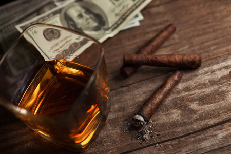 Cigarettes, money and glass with brandy on the tableの写真素材