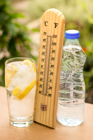 Ice cubes in a glass of water with thermometer and water bottleの写真素材