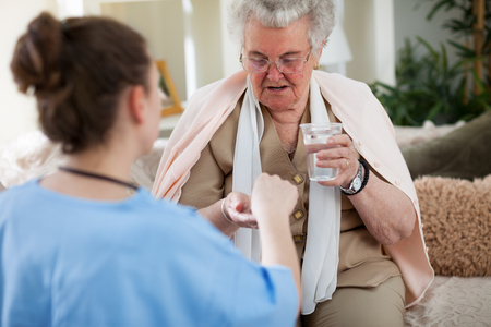 Nurse giving medicines and providing help to old womanの写真素材