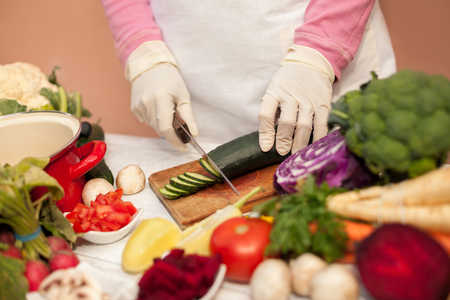 Woman with gloves slicing cucumber on cutting boardの写真素材