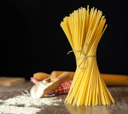 Raw tied spaghetti and wooden scoop with flour on wooden surfaceの写真素材