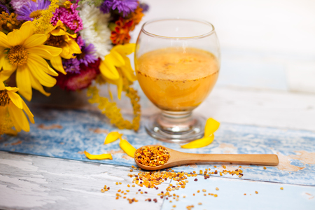 Bee pollen in wooden spoon with glass of liquid pollen behind it on the tableの写真素材