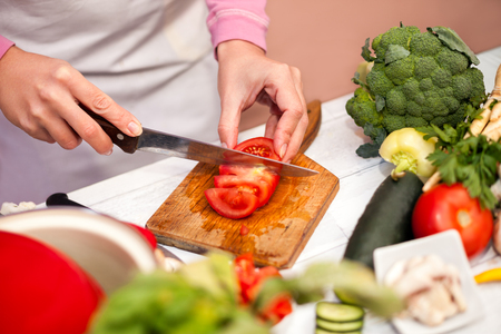Cutting tomato on slices, woman preparing vegetable in the kitchen for saladの写真素材