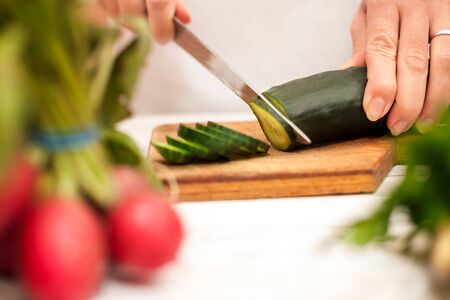 Housewife slicing cucumber in the kitchen with a knifeの写真素材