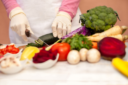 Woman with white glove slicing cucumber and preparing vegetable on chopping board in the kitchenの写真素材