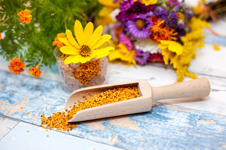 Pollen in wooden scoop with yellow flower in plastic glass on the tableの写真素材