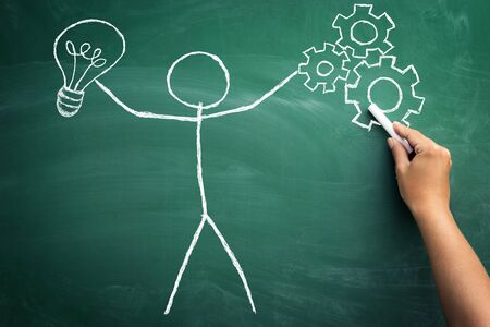 Stickman with bulb and gear mechanism in his hands on blackboardの写真素材