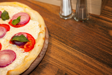 Pizza with basil and tomato on the top on wooden tableの写真素材