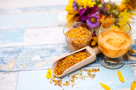 Pollen in wooden scoop and glasses on the table with flowers in the backgroundの写真素材