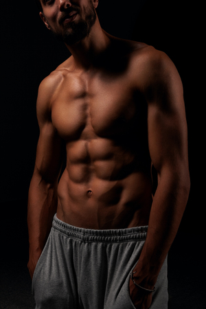 Young man showing his six pack abs with his hand in the pockets and posing on black backgroundの写真素材