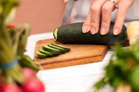 Housewife cutting cucumber with a knife in the kitchen on cutting board