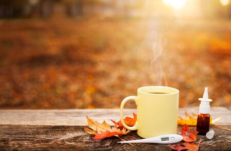 Cup with hot tea and thermometer showing high temperature along with nose drops on wooden surface, flu season in autumnの写真素材