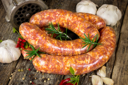 Raw sausages with rosemary, garlic, chili peppers and peppercorn on wooden surfaceの写真素材