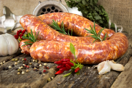 Raw sausages with rosemary and peppercorn on wooden tableの写真素材