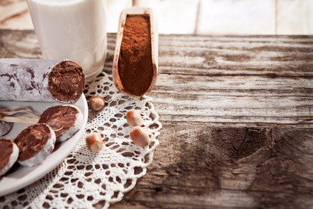 Top view on wooden scoop with cocoa and chocolate sausage on plate and hazelnuts on the tableの写真素材