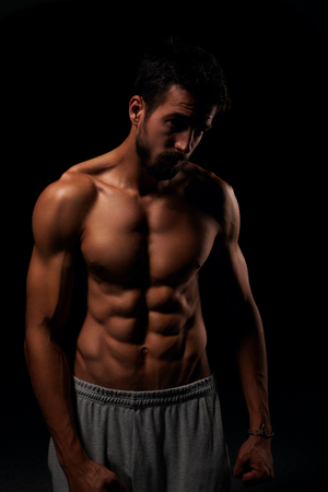 Attractive shirtless man showing his six pack and posing on black backgroundの写真素材