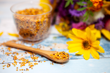 Focused spoon with pollen on the table, glass with pollen and colorful flower in the backgroundの写真素材