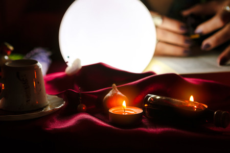 Crystal ball and candles for fortune telling with bottle on red sheetの写真素材