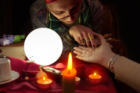 Old fortune teller woman holding another woman hand for palm readingの写真素材