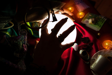 Gypsy woman fortune teller put her hand on crystal ball and concentrate on predictionの写真素材