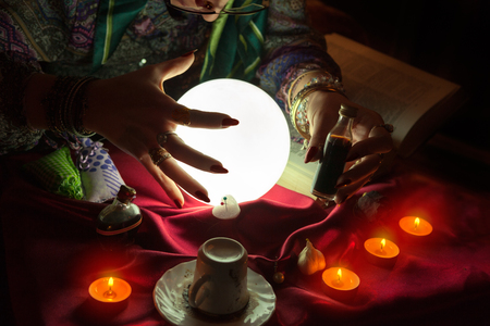 Love potion in hand of fortune teller woman and her hand above crystal ballの写真素材