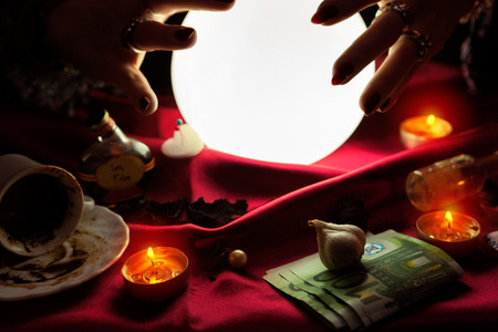 Hands of fortune teller around glowing crystal ball