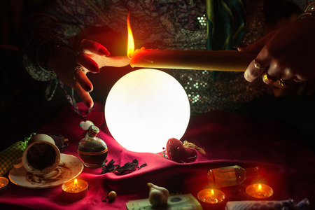 Candle in hand of fortune teller woman above illuminated crystal ballの写真素材
