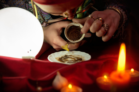 Woman fortune teller looking in empty coffee cup and reads futureの写真素材