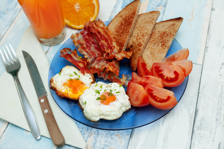 Delicious fried eggs,bacon,toast and tomatoes on plateの写真素材