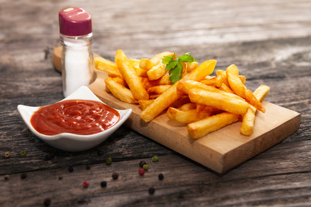 French fries on chopping board with bowl of tomato sauceの写真素材
