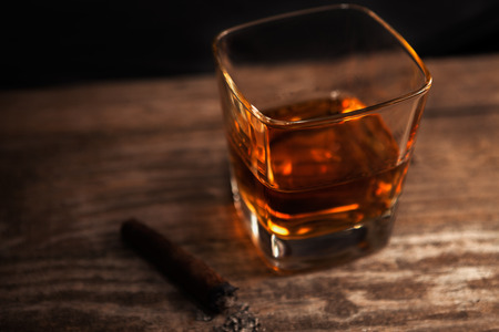 Glass with whiskey and cigar with ashes on the tableの写真素材