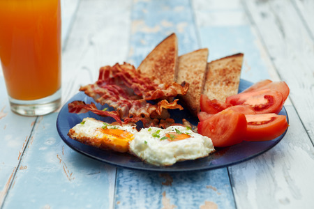 Breakfast with fried eggs, bacon, tomatoes and toast on wooden tableの写真素材