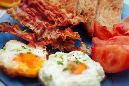Close shot of breakfast with fried eggs, bacon and tomato on a plateの写真素材