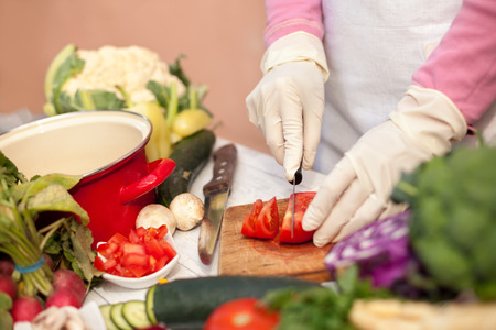 Female with gloves cutting tomato on cutting boardの写真素材