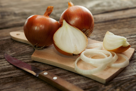 Fresh onion and onion cuts on chopping board with a kitchen knifeの写真素材