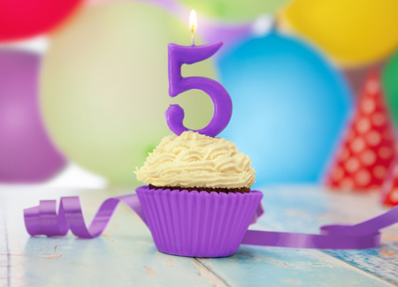 Birthday candle with number 5 on birthday cupcake with balloons in the backgroundの写真素材