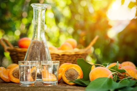 Fruit brandy in a glass and apricots on wooden tableの写真素材