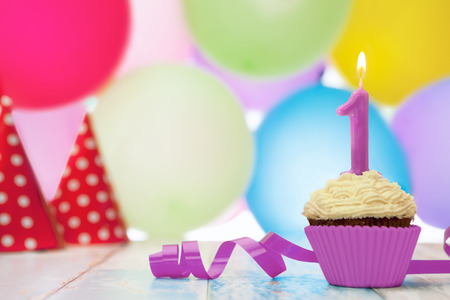 Delicious cupcake dessert for birthday with candle and hats in the backgroundの写真素材
