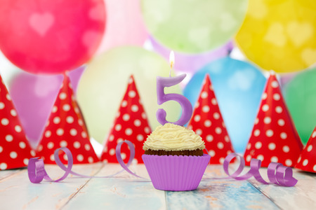 Muffin with candle in number 5 shape and party hats in the backgroundの写真素材