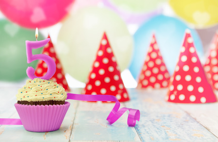 Cupcake with candle, party hats and balloons in the backgroundの写真素材