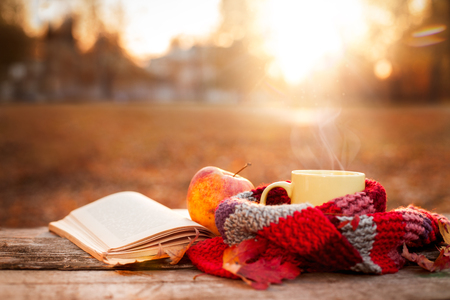 Open book, apple and yellow tea mug with warm scarf on wooden surfaceの写真素材