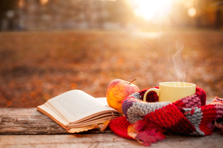 Open book, apple and yellow tea cup with warm scarf on wooden surfaceの写真素材