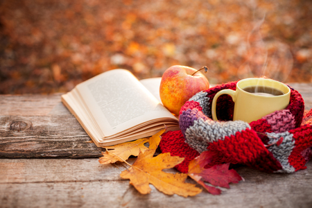 Yellow tea cup with warm scarf open book and apple on wooden surfaceの写真素材